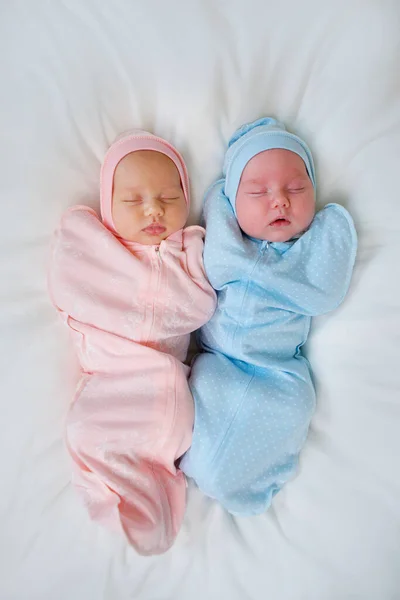 Two newborn baby twins boy and girl are in pink and blue suits on a white blanket.