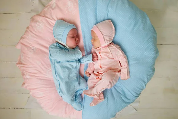 Two newborn baby twins boy and girl are in pink and blue suits on a white blanket.