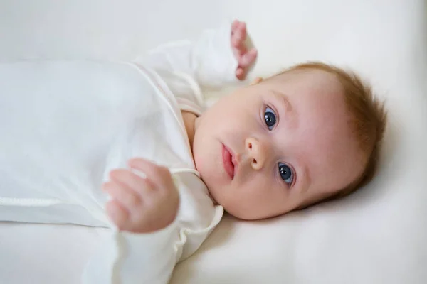 Little newborn baby girl lying in white clothes on white background.