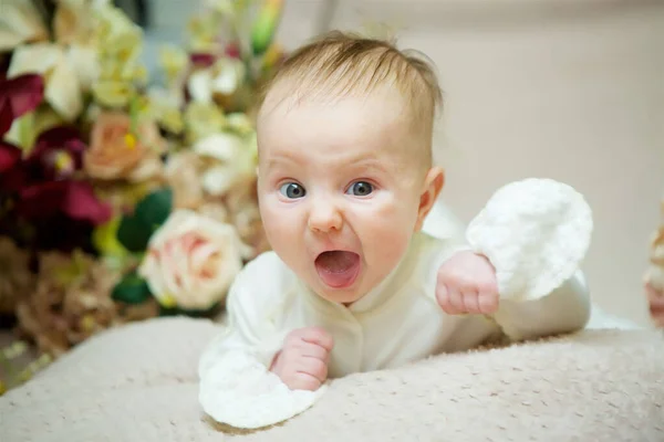 Little newborn baby girl lying on her tummy in white clothes on a beige blanket. On the face of the child emotion of aggression.