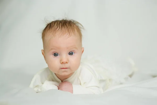Little newborn baby girl lying in white clothes on white blanket background.