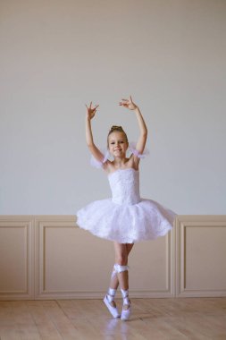 Beyaz etekli küçük kız balerin bale sınıfında yerde yatıyor..