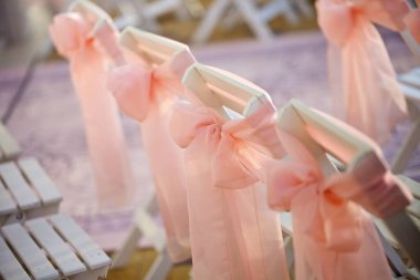 Sandalyeler sıraya dizilmiş ve düğün töreni için pembe kurdelelerle süslenmiş..