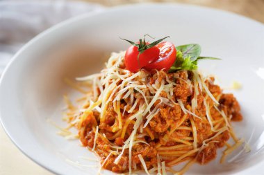 İtalyan mutfağı. Etli domatesli makarna ve fesleğen yaprakları tahta bir tabakta üç kırmızı domatesin yanında servis ediliyor.