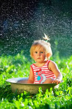 Bir çocuk doğada bir havuzda banyo yapar. Gün batımı. Kırmızı çizgili mayo giyen bir kız..