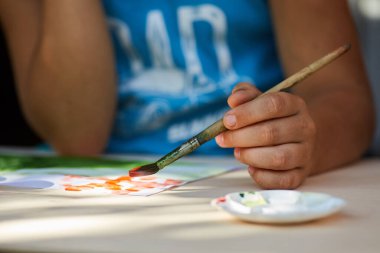 Çocuğun eli gouache boyalarıyla bir resim çiziyor. Sanat ve çocuk yaratıcılığı kavramı.