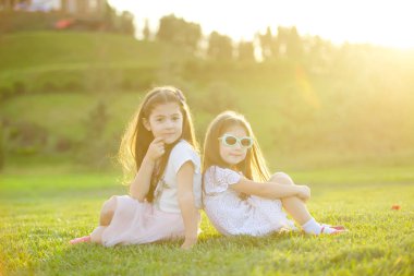 Batan güneşin altında çimlerin üzerinde iki kız oturuyor. Doğa ve yaz tatilleri.