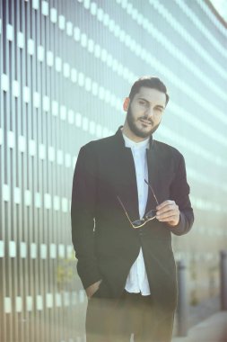 Başarılı bir temsilci, modern binanın önünde duran sakallı, zengin ve modaya uygun bir adam. Erkekler için güneş gözlüğü.