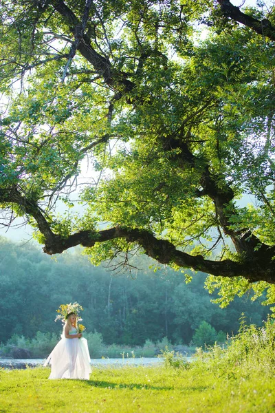 妖精をイメージした学齢の少女が大きな広がりの木の下の川の清掃に立っている 魔法とおとぎ話 — ストック写真
