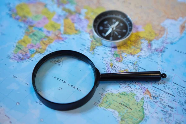 The magnifying glass is located on the world map and magnifies the Indian ocean. There\'s a compass next to it. Concept of travel and news about the selected geographical area.