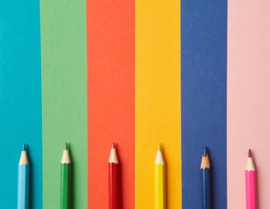 Çeşitli tonlarda çeşitli renkli kalemler her biri kendi renginde, çeşitli tonlarda parlak renkli bir arka planda yatar. Eğitim ve sanatsal yaratıcılık kavramı.