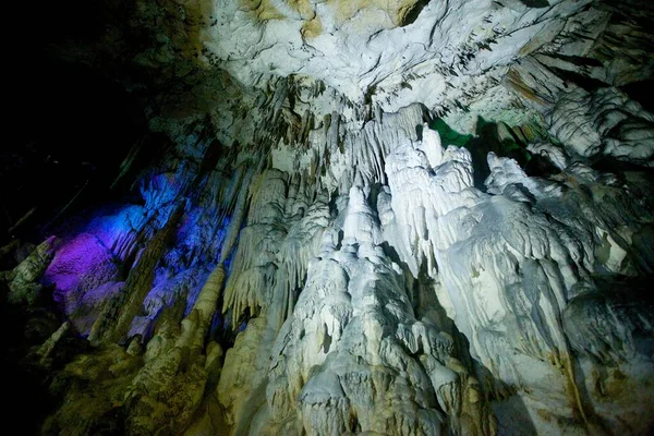 Dark cave view from inside with a lumen. Stalactites and stalagmites inside the stone grotto. Colorful stones in the cave. Lighting electricity beauty of the cave.