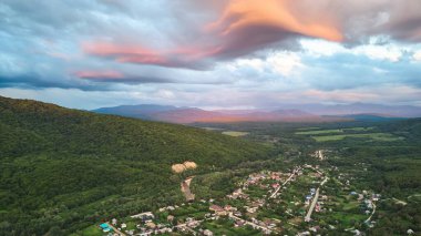 Dağların eteklerinde ve nehir kıyısında küçük bir köy. Gün batımı zamanı. Yılın bu zamanı yaz..