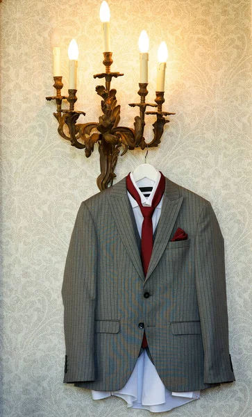 A gray men\'s suit is hanging on a hanger. A white shirt and a red tie. Men\'s fashion.