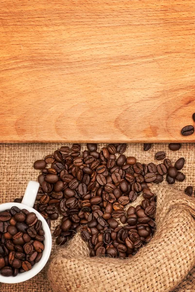 Разбросанные зерна кофе, чашки с зерном и деревянная доска — стоковое фото