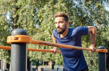 Düz olmayan çubuklarda şınav çeken bir adam. Spor salonu aç. Belediye spor simülatörleri üzerine sokak eğitimi. 