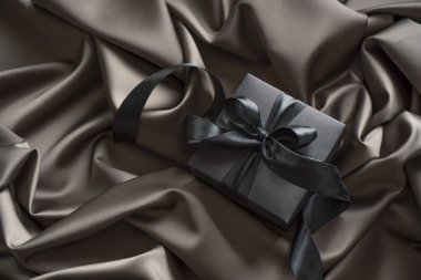 Saten çarşafların üzerinde siyah kurdele olan siyah hediye kutusu..