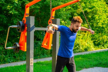 Açık hava geçiş makinesi. Şehir parkındaki açık hava spor salonunda eğitim aletlerini iten adam..