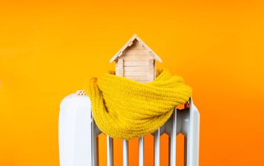 Kış konseptine göre evde soğuk. İkamet yeri fikrinin ısıtma verimliliği zayıf. Elektrikli kaloriferin üzerinde duran yün bir eşarba sarılı oyuncak ahşap evden yapılmıştır..