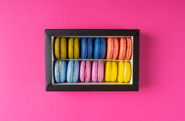 Makarnaların üst görüntüsü. Pembe arka planda kağıt kutuda renkli kurabiyeler..