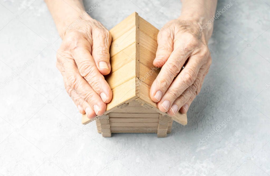 Wrinkled hands of an elderly woman protects the house. Taking care of your home concept.