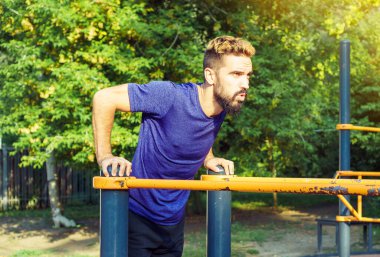 Karizmatik bir adam yaz parkında düz olmayan barlarda şınav çekiyor..