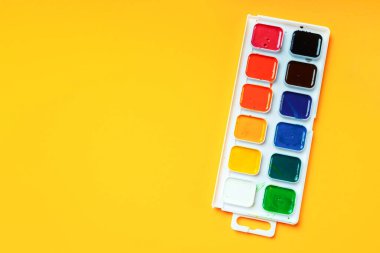 Sarı arka planda suluboya boyalı palet, üst manzara, kopyalama alanı. Çocukların yaratıcı ve sanat eğitimi konsepti.