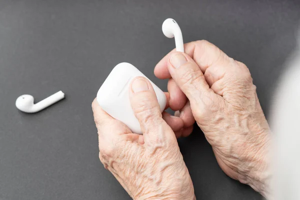 Elderly people use a modern technology. Concept with an old wrinkled hands holding a bluetooth earphones.