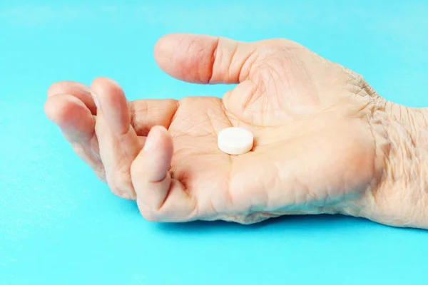 Old wrinkled hand holding pill on a blue background.