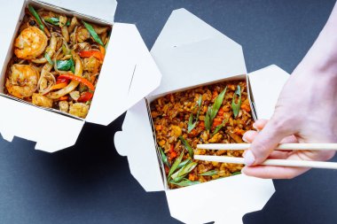 Wok kutuları. Deniz mahsullü Asya cam eriştesi ve sebzeli pilav. Dişi el yemek çubuklarını tutuyor ve pilav alıyor. Üst görünüm.