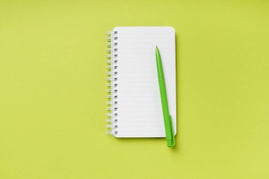 Fotokopi alanı olan yeşil bir arka planda boş bir not defteri ve kalem. Üst görünüm.