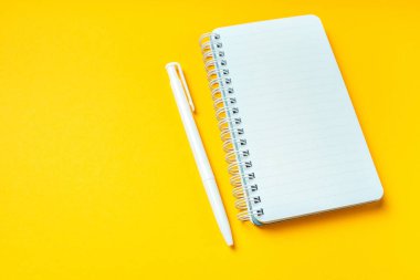 Kopya alanı olan sarı arkaplanda boş bir not defteri ve kalem. Üst görünüm.