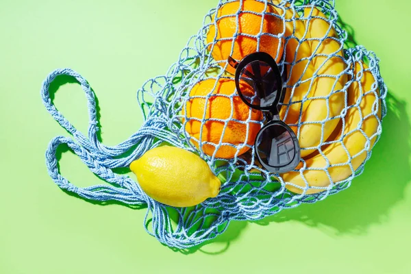 Zero waste trendy shopping mesh bag with fruits on a grenn bakground.