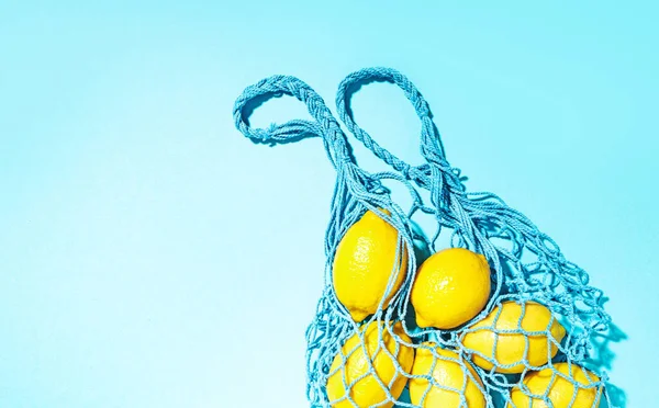 Mesh bag filled with lemons on a blue background.