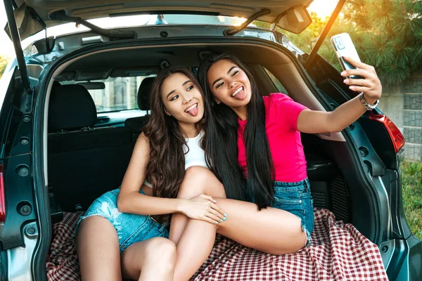 Two Pretty Asian Girls Sitting Car Trunk Showing Tongues While — Foto Stock
