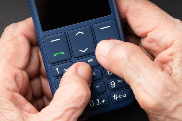 Old wrinkled hands holding a push-button mobile phone with big buttons. Elderly using cell phone concept.