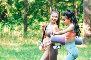 Two pretty asian ladies rush to morning workout at the open air. Yoga practise, stretching or fitness in the open air.