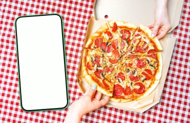 Pizza, hands and empty cellphone for your app design. Blank empty smartphone with white screen near the hands holding pizza slices. View above. 