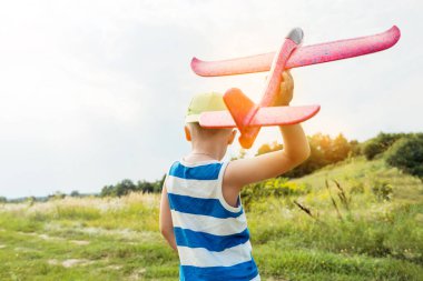 Boy holding toy airplane and preparing to launch it into the sky outdoors. Happy childhood, dreaming concept.