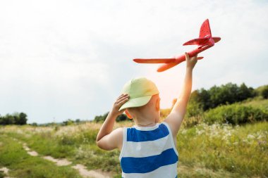 Boy holding toy airplane and hat preparing to launch plane into the sky outdoors. Happy childhood, dreaming concept.