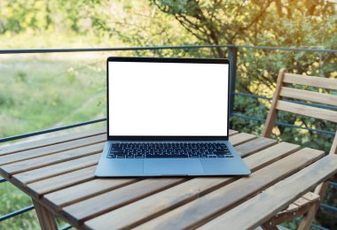 Modern blank laptop with white screen for your advertising on the wooden table on a fresh air.