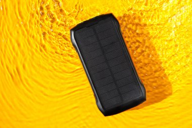Portable powerbank with solar panel lies by the water, accumulates solar energy during traveling. Alternative eco energy producing.