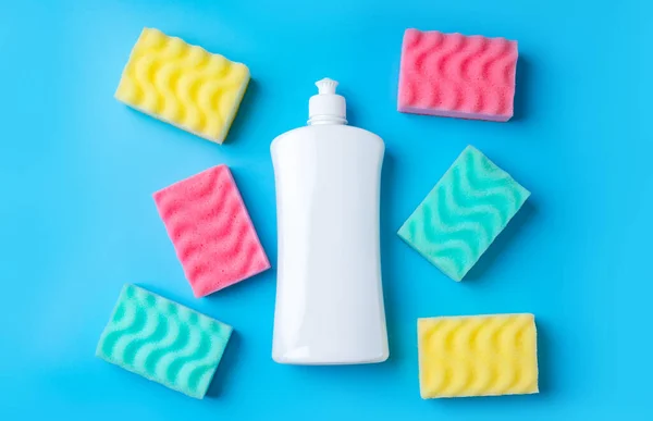 Empty plastic bottle with cleaning detergent and colorful sponges on a blue background.