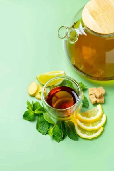 Tea time. Composition made with double wall glass of tea, transparent teapot, mint, lemon, ginger, cane sugar. Vertical photography.