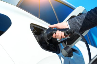 Elektrikli araba şarj oluyor. Adamın eli, elektrikli arabanın elektrik bağlantısını yerleştiriyor. Yeşil enerji, çevre dostu yakıt.