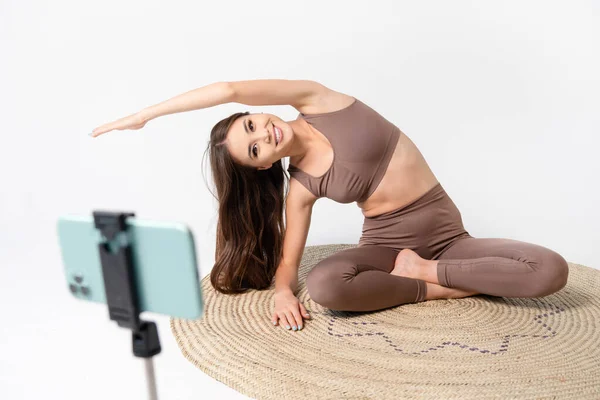 ヨガオンライン オンライントレーニング自宅でフィットアジアの女性と床に座っている三脚に保持している携帯電話に対して — ストック写真