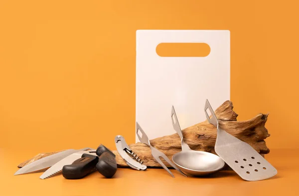 Camping kitchen utensils for cooking outdoors lying on a weathered wooden log.
