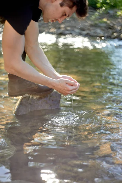 Male traveller taking break at river during hike. Tired guy washing face with river water — Stock Photo, Image