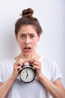 Şaşırmış bir kadın sabahın köründe elinde çalar saatleri elinde tutuyor.