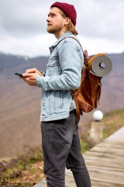 Genç, yakışıklı, vahşi, sakallı adam cep telefonu kullanarak vahşi doğada geziyor.